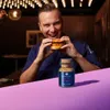 A man in a chef's uniform is about to eat a burger, with a spice jar in the foreground. Produktbild-Vorschau