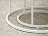 A close-up view of the white metal base of a table, resting on a patterned rug. Náhľad obrázku produktu