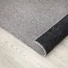 A close-up view of a gray rug with a rolled-up edge, lying on a light wooden floor. Produktbild-Vorschau