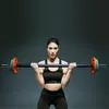 A woman is holding a barbell in a gym setting. Náhľad obrázku produktu
