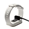 A white smart band is shown connected to a black charging cable. Náhled obrázku produktu