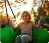 A young girl is happily swinging on a large, round swing outdoors during sunset. Podgląd zdjęcia produktu