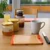 A breakfast setting with jars of jam and honey, a glass of juice, a mug, and a cutting board on a wooden table. Produktbild-Vorschau