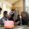 A group of people are gathered around a table in an office setting, looking at a tablet. An aroma diffuser is placed on the table in the foreground. Anteprima dell’immagine prodotto