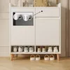 A white cabinet with storage compartments and shoe racks, showing two chrome knobs on the left side. The cabinet is made of composite material and wood. Náhled obrázku produktu