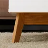 A close-up view of the leg and underside of a white and wood coffee table, resting on a cream-colored rug. Produktbild-Vorschau