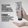 A hand holding a tube of Redken Hair Cleansing Cream Shampoo, with product dispensing into the palm. Náhled obrázku produktu