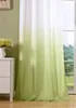 A close-up view of a green and white gradient curtain hanging in front of a window. Produktbild-Vorschau