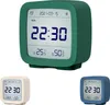 A collage of three digital alarm clocks in different colors (green, beige, and blue) against a white background. The green clock is prominently displayed in the center, showing the time, date, temperature, and humidity. Podgląd zdjęcia produktu