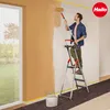 A man is painting a wall while standing on a stepladder. There is a bucket and paint roller on the floor. Anteprima dell’immagine prodotto