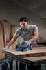 A man is using a power planer on a large piece of wood in a workshop. Produktbild-Vorschau