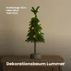 A small, decorated Christmas tree with lights on a wooden surface. Produktbild-Vorschau