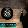 A person is about to throw a dart at a dartboard mounted on a wooden wall. Podgląd zdjęcia produktu