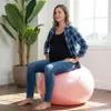 A pregnant woman is sitting on a pink exercise ball in a room with a large plant and a window. Náhled obrázku produktu