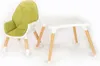 A green and white high chair and a white table with wooden legs are shown against a white background. Produktbild-Vorschau