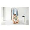A woman is sitting on the floor in front of a clothing rack and a dehumidifier. Podgląd zdjęcia produktu