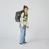 A young girl wearing a backpack stands against a white background. Produktbild-Vorschau