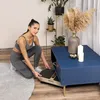 A woman in workout clothes is interacting with a vibration plate next to a blue coffee table. Náhled obrázku produktu