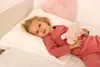 A young girl lies in bed with a stuffed unicorn. Produktbild-Vorschau