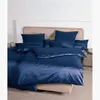 A neatly made bed with navy blue satin bedding and several pillows.