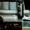 A bottle of K2 APC STRONG PRO cleaner is being held over a car seat that is partially cleaned, showing a contrast between the dirty and clean areas. A measuring cup with liquid and a brush are also visible. Náhled obrázku produktu