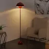 A red floor lamp is shown in a room with a beige armchair and a small side table with a plant. Anteprima dell’immagine prodotto