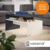 A modern coffee table with storage, placed on a fluffy rug in a living room setting. Produktbild-Vorschau