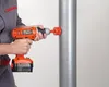 A person is using a cordless drill with a hole saw attachment to drill a hole in a large metal pipe. Náhled obrázku produktu