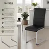 A black dining chair with a silver frame is shown in a modern dining room setting, next to a white table with a plant and a mug on it. Produktbild-Vorschau