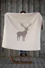 A person is holding up a blanket with a deer print in front of a wooden wall, standing on a sled. Produktbild-Vorschau