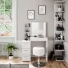 A white vanity table with a mirror and stool, decorated with framed art and shelves filled with cosmetics, set in a bright room with a large window. Náhled obrázku produktu