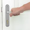 A hand is shown gripping a silver door handle on a white door. Náhľad obrázku produktu