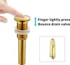 A finger pressing down on a gold pop-up drain valve for a sink, with an inset image of the internal mechanism. Produktbild-Vorschau