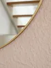 A close-up view of a round mirror with a gold rim and a textured pink surface. In the background, a staircase with wooden steps is visible. Produktbild-Vorschau