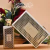 A perfume bottle and its box are displayed with flowers in the background. Anteprima dell’immagine prodotto