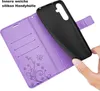 A hand is holding a black phone case over an open purple wallet case with card slots and a floral butterfly design. Produktbild-Vorschau