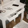 A close-up view of a white vanity table with makeup and a smartphone on top, and open drawers revealing makeup and a candle. Podgląd zdjęcia produktu