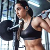 A woman is lifting weights in a gym while wearing Bluetooth sport headphones. Produktbild-Vorschau
