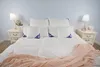 A neatly made bed with white bedding, decorative pillows, and a pink throw blanket. Produktbild-Vorschau