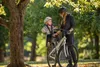 A woman and a child are standing next to a bicycle in a park. Anteprima dell’immagine prodotto