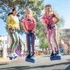 A woman and two girls are jumping on pogo sticks in an outdoor playground. Produktbild-Vorschau