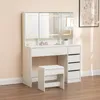 A white vanity table with LED lights, mirrors, drawers, and a stool, set against a light pink wall and wooden floor. Produktbild-Vorschau