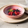 A pink ceramic bowl filled with raspberries and blackberries sits on a wooden tray. Náhled obrázku produktu