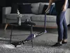 A person is using a cordless vacuum cleaner in a living room. Produktbild-Vorschau
