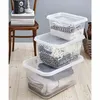 Three transparent storage boxes are stacked on a wooden floor, with a chair and books in the background. Voir les images du produit