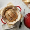 A loaf of bread in a red Dutch oven, with a bread knife and a lid nearby. Anteprima dell’immagine prodotto