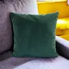 A green corduroy pillow is placed on a gray sofa, with a yellow sofa in the background. Produktbild-Vorschau