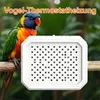A colorful parrot is perched on a branch next to a white heating device with many small holes. Produktbild-Vorschau