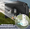 A black pop-up tent set up in a grassy field with sunlight rays shining on it. Inside the tent, there is a campfire and two people. A close-up inset shows the base of a tent pole with stakes. Produktbild-Vorschau