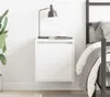 A white wall-mounted nightstand with a lamp and a cup on top, next to a bed. Náhled obrázku produktu